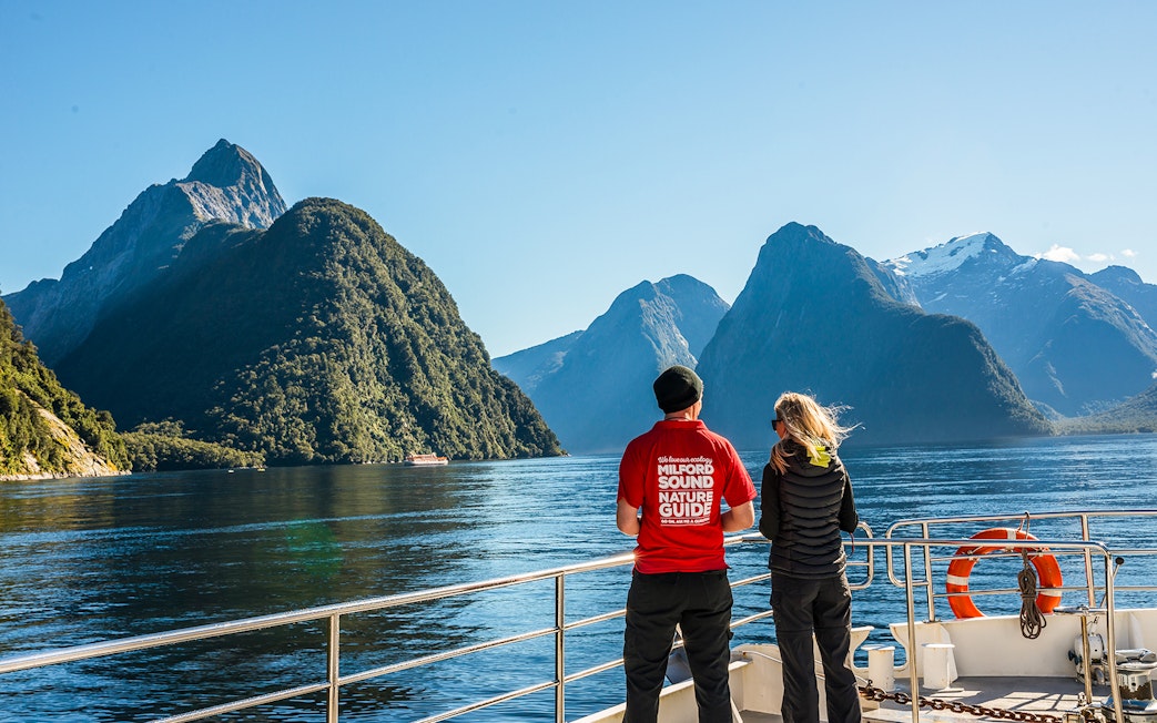 Passenger with nature guide on Milford Sound cruise, viewing scenic fjords and mountains.
