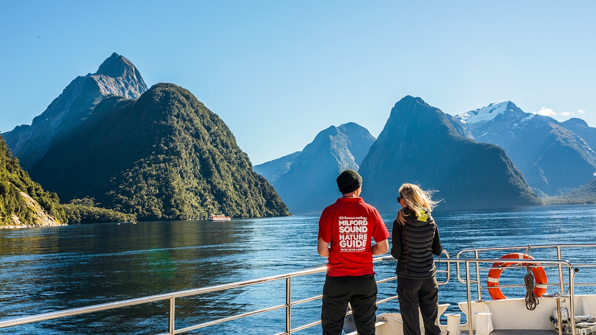 Passenger with nature guide on Milford Sound cruise, viewing scenic fjords and mountains.
