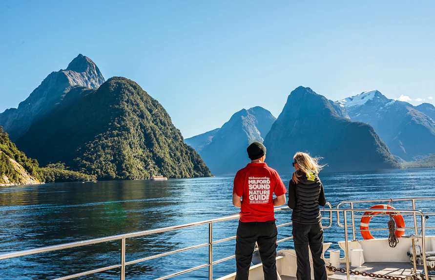 Passenger with nature guide on Milford Sound cruise, viewing scenic fjords and mountains.