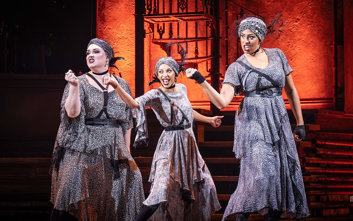 Performers in Hadestown musical on stage with dramatic expressions.