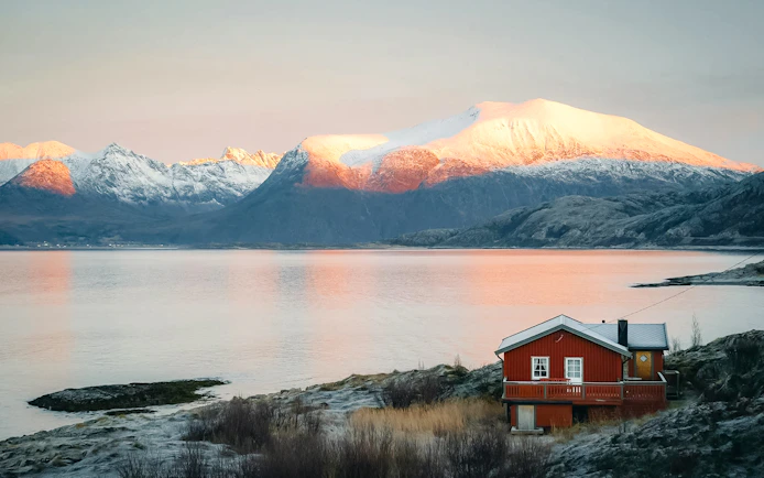 Red cabin by Sommarøy Fjord with snow-capped mountains, Tromsø.