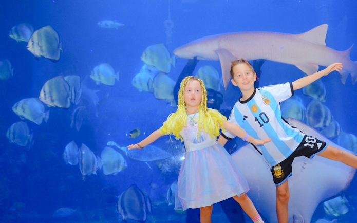 Children posing in front of a large aquarium tank at Hurghada Grand Aquarium.