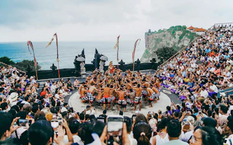 Kecak dance performance at Bali amphitheater with ocean view and audience.