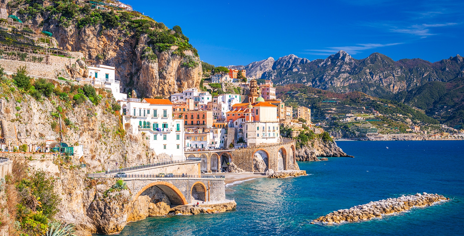Coastal view of Sorrento, Italy, with colorful buildings on cliffs and tourists by the sea.