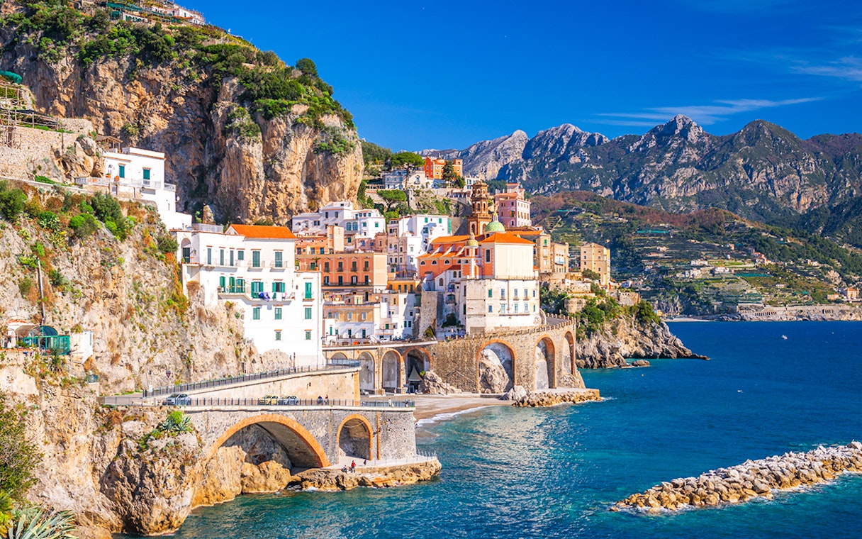 Coastal view of Sorrento, Italy, with colorful buildings on cliffs and tourists by the sea.