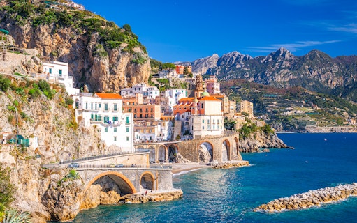 Coastal view of Sorrento, Italy, with colorful buildings on cliffs and tourists by the sea.