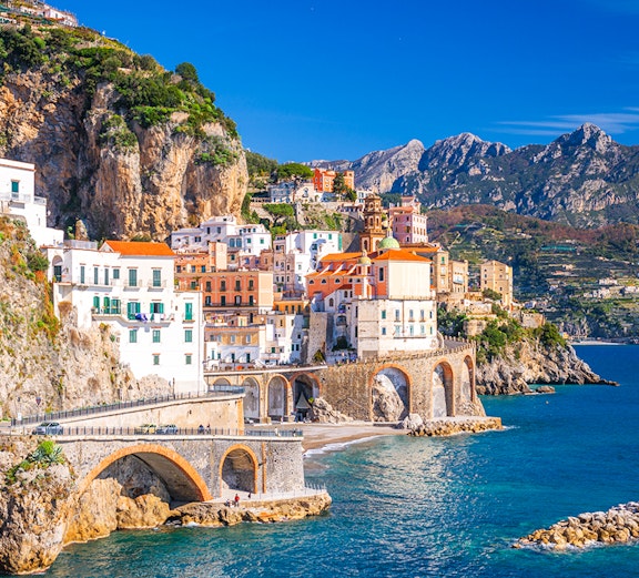 Coastal view of Sorrento, Italy, with colorful buildings on cliffs and tourists by the sea.