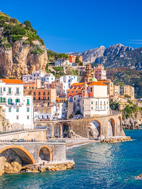 Coastal view of Sorrento, Italy, with colorful buildings on cliffs and tourists by the sea.