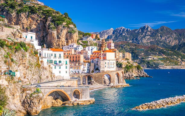 Coastal view of Sorrento, Italy, with colorful buildings on cliffs and tourists by the sea.