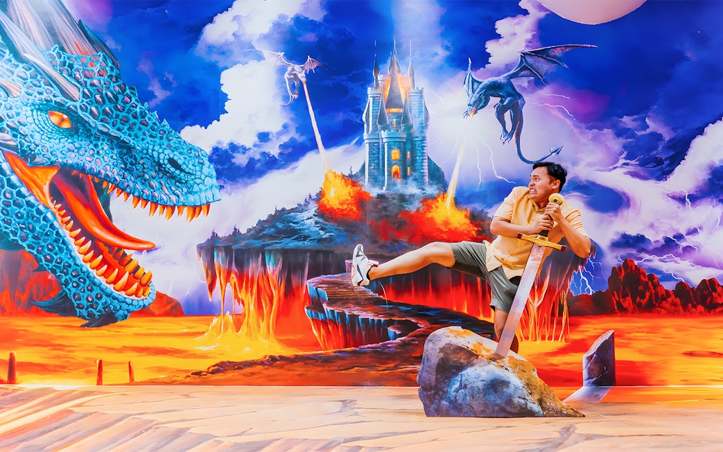 Man posing with sword in fantasy dragon mural at Trick Eye Museum, Singapore.