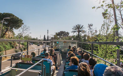 Barcelona hop-on hop-off bus with tourists, palm trees, and city street.