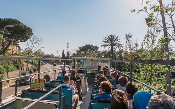 Barcelona hop-on hop-off bus with tourists, palm trees, and city street.