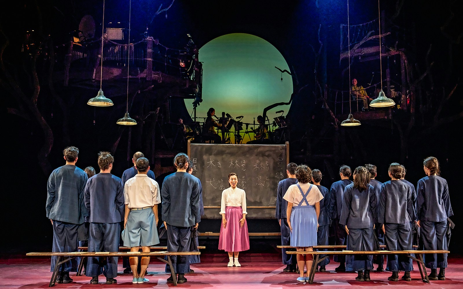Stage performance of My Neighbour Totoro with actors in front of a chalkboard and musicians in the background.