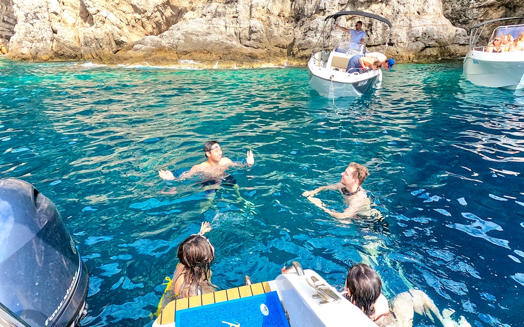 Guests swimming near boats in the blue waters of coastal caves.