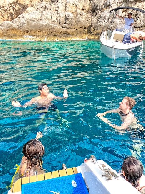 Guests swimming near boats in the blue waters of coastal caves.