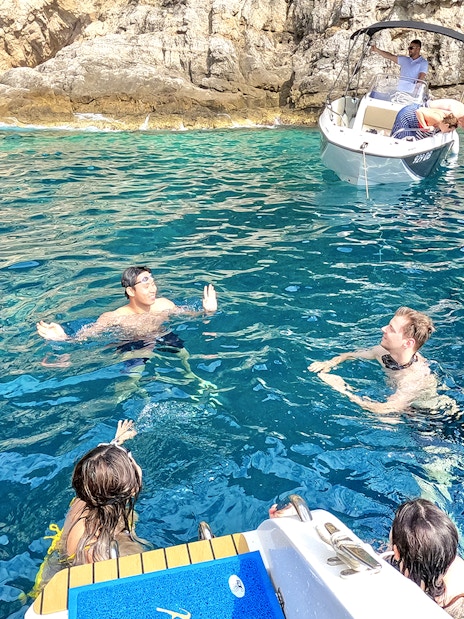 Guests swimming near boats in the blue waters of coastal caves.