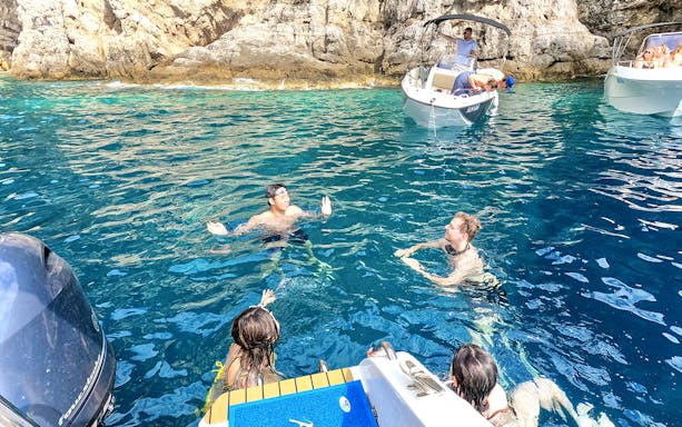 Guests swimming near boats in the blue waters of coastal caves.