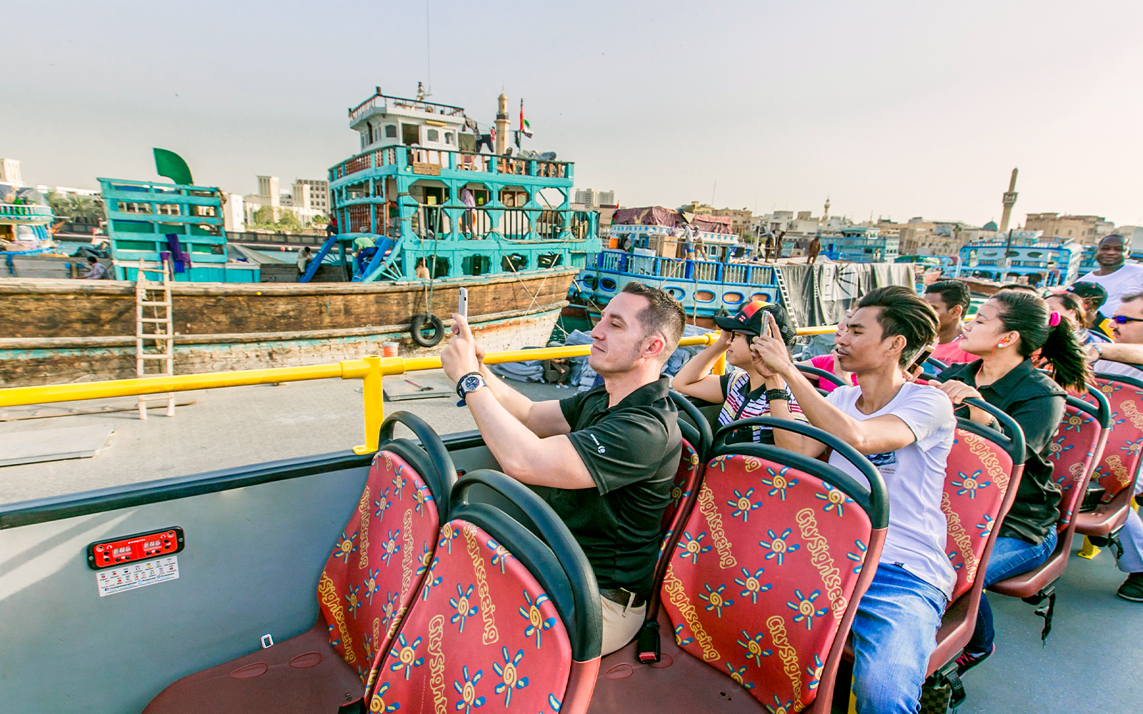 Tourists on a hop-on hop-off bus taking photos of Al Seef Dhow in Dubai.