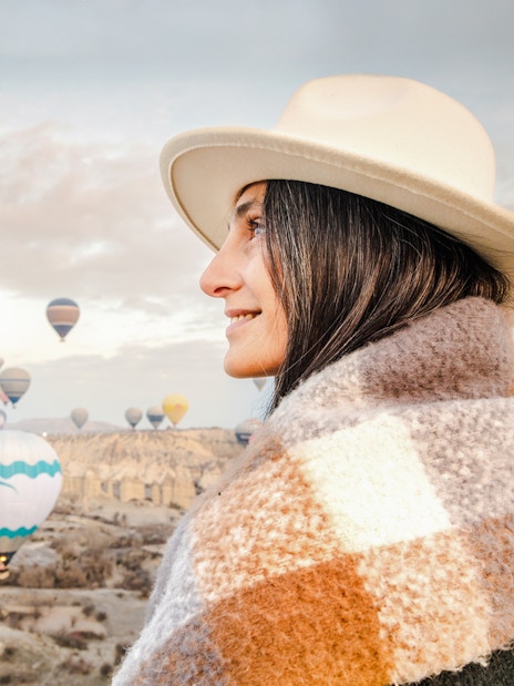 Woman in fedora and shawl gazing at hot air balloons in Cappadocia, Turkey.