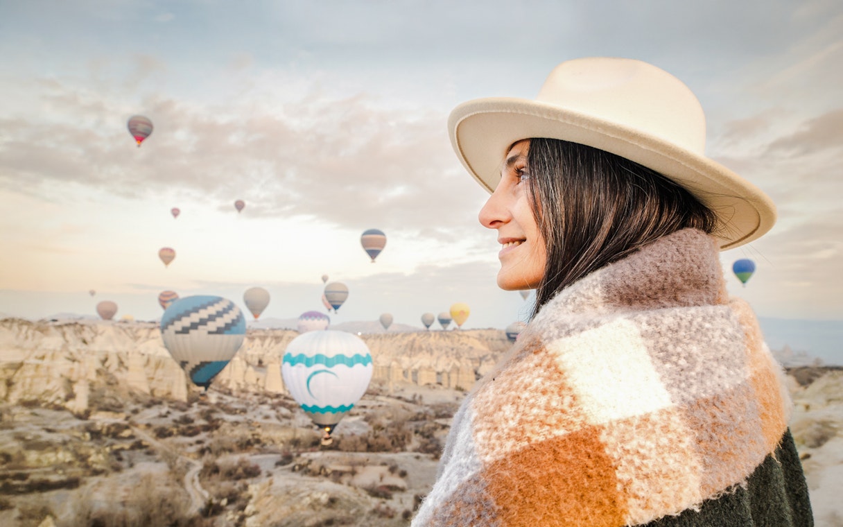 Woman in fedora and shawl gazing at hot air balloons in Cappadocia, Turkey.