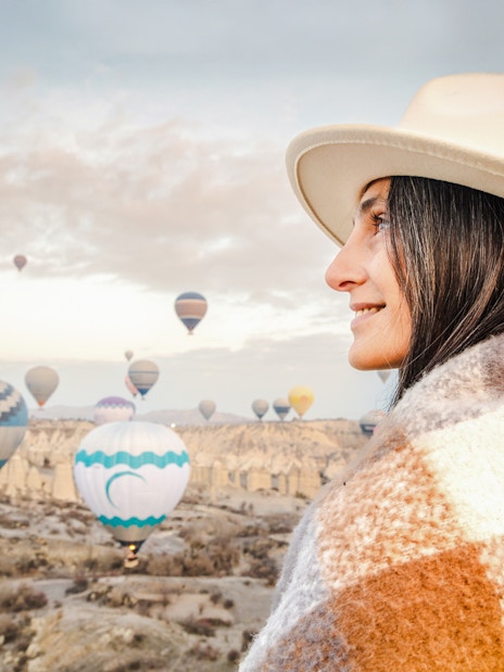 Woman in fedora and shawl gazing at hot air balloons in Cappadocia, Turkey.
