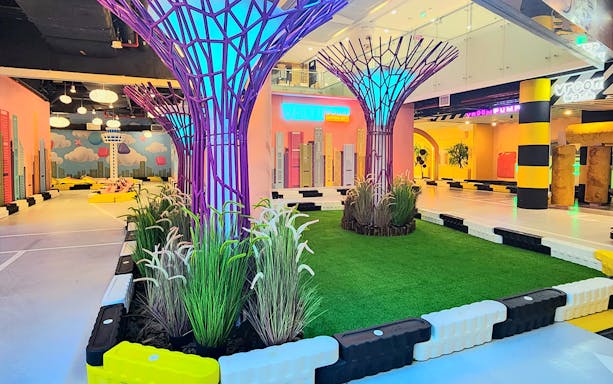 Neon-lit driving course with tree-like sculptures at VroomTown Driving City.