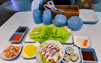 Korean BBQ side dishes with lettuce, kimchi, pickled radish, and sushi rolls on Phu Quoc Sunset Tour.