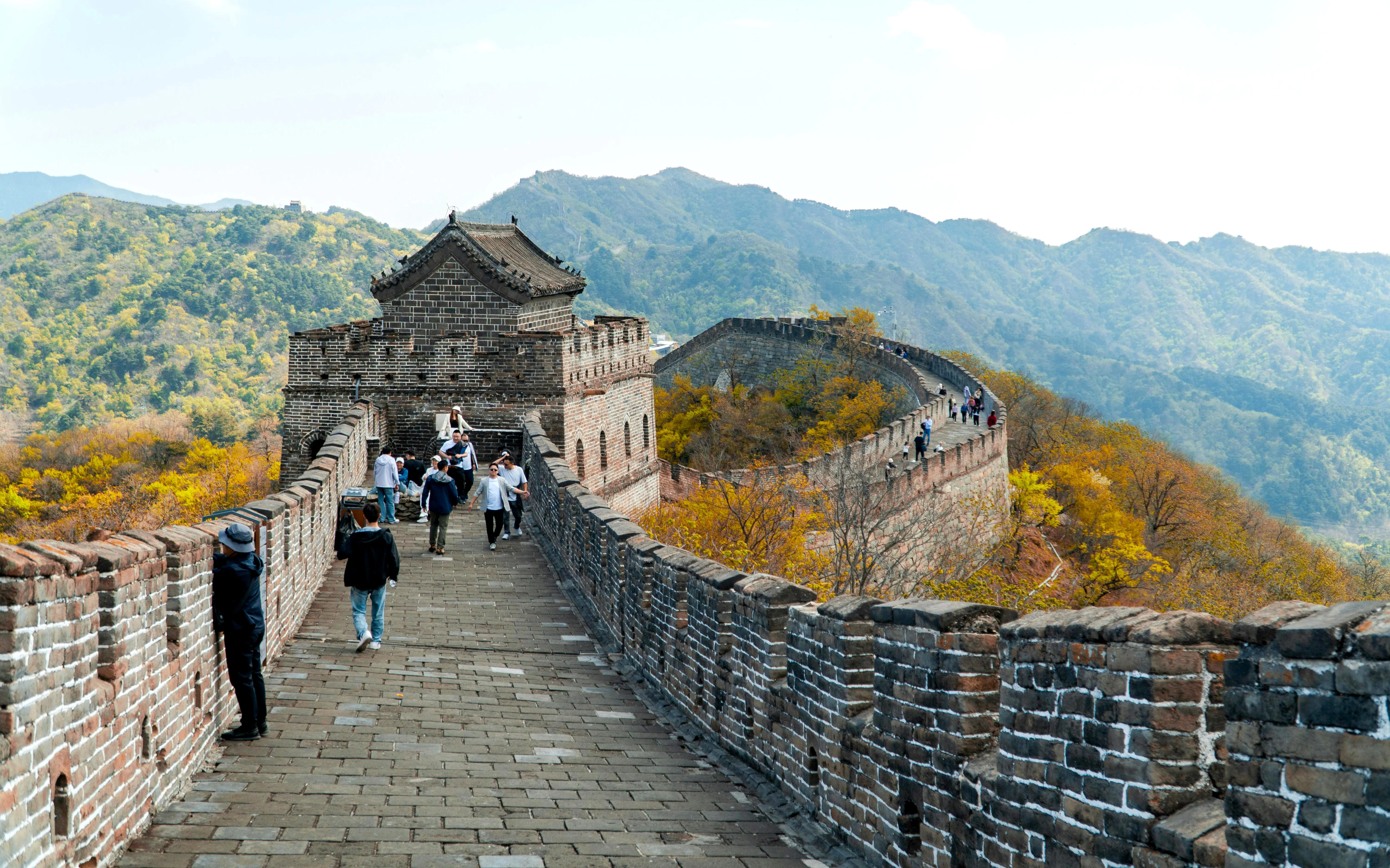 Visitors walking along the Mutianyu section of the Great Wall of China, surrounded by mountains.