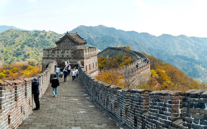 Visitors walking along the Mutianyu section of the Great Wall of China, surrounded by mountains.