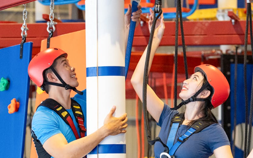 Participants in harnesses navigating an indoor ropes course.