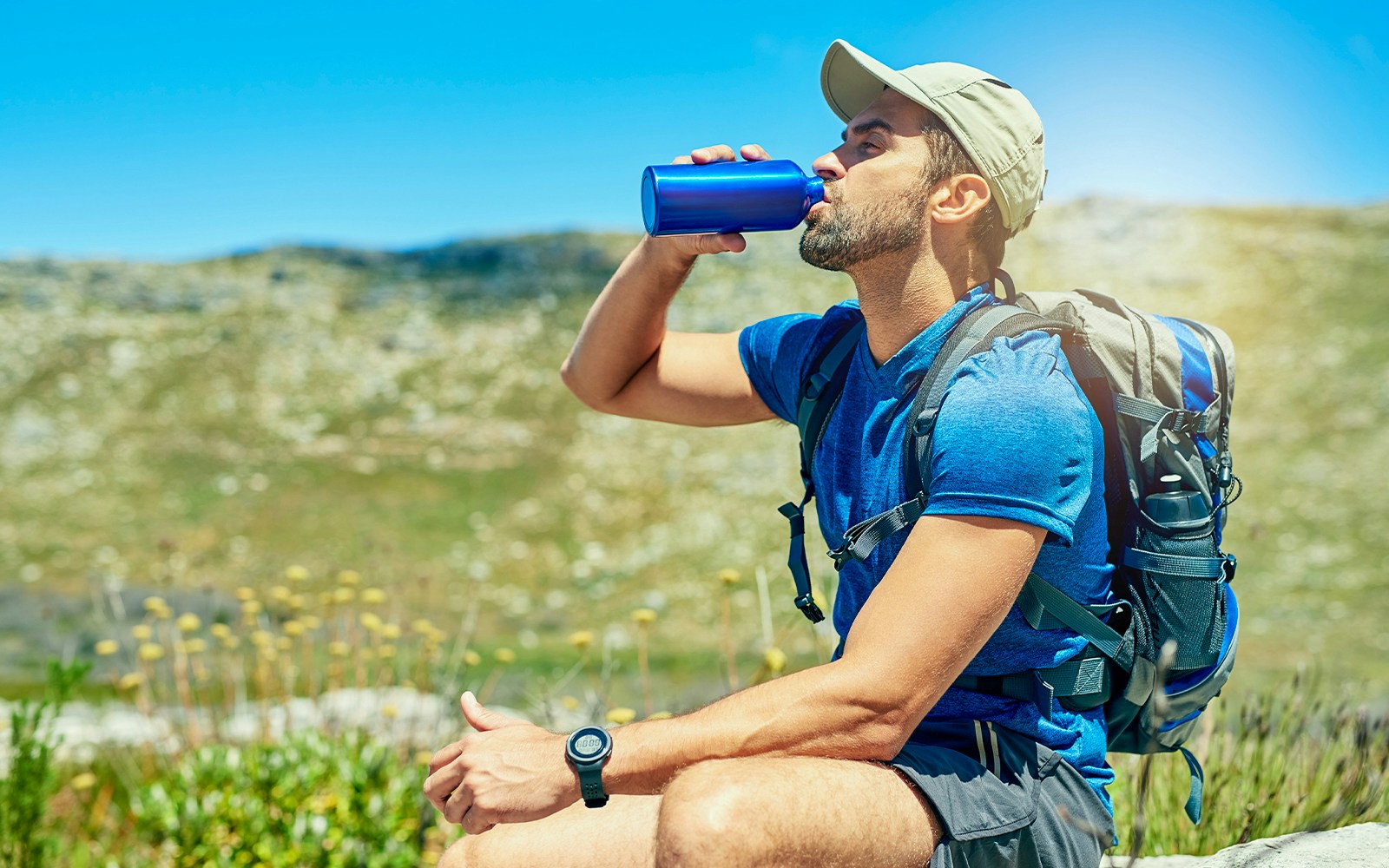 Man drinking water from a bottle while hiking in a mountainous area.