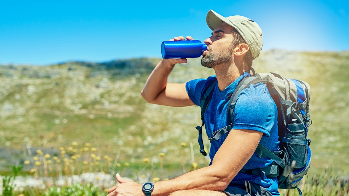 Tourist drinking water from a bottle in a sunny outdoor setting, emphasizing hydration.