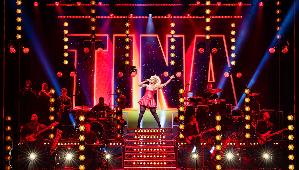 Performer on stage during TINA – The Tina Turner Musical with band and vibrant lights.