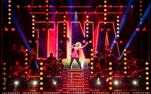 Performer on stage during TINA – The Tina Turner Musical with band and vibrant lights.