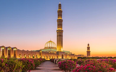 Sultan Qaboos Grand Mosque in Muscat at sunset with gardens in the foreground.