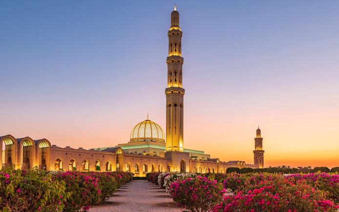 Sultan Qaboos Grand Mosque in Muscat at sunset with gardens in the foreground.