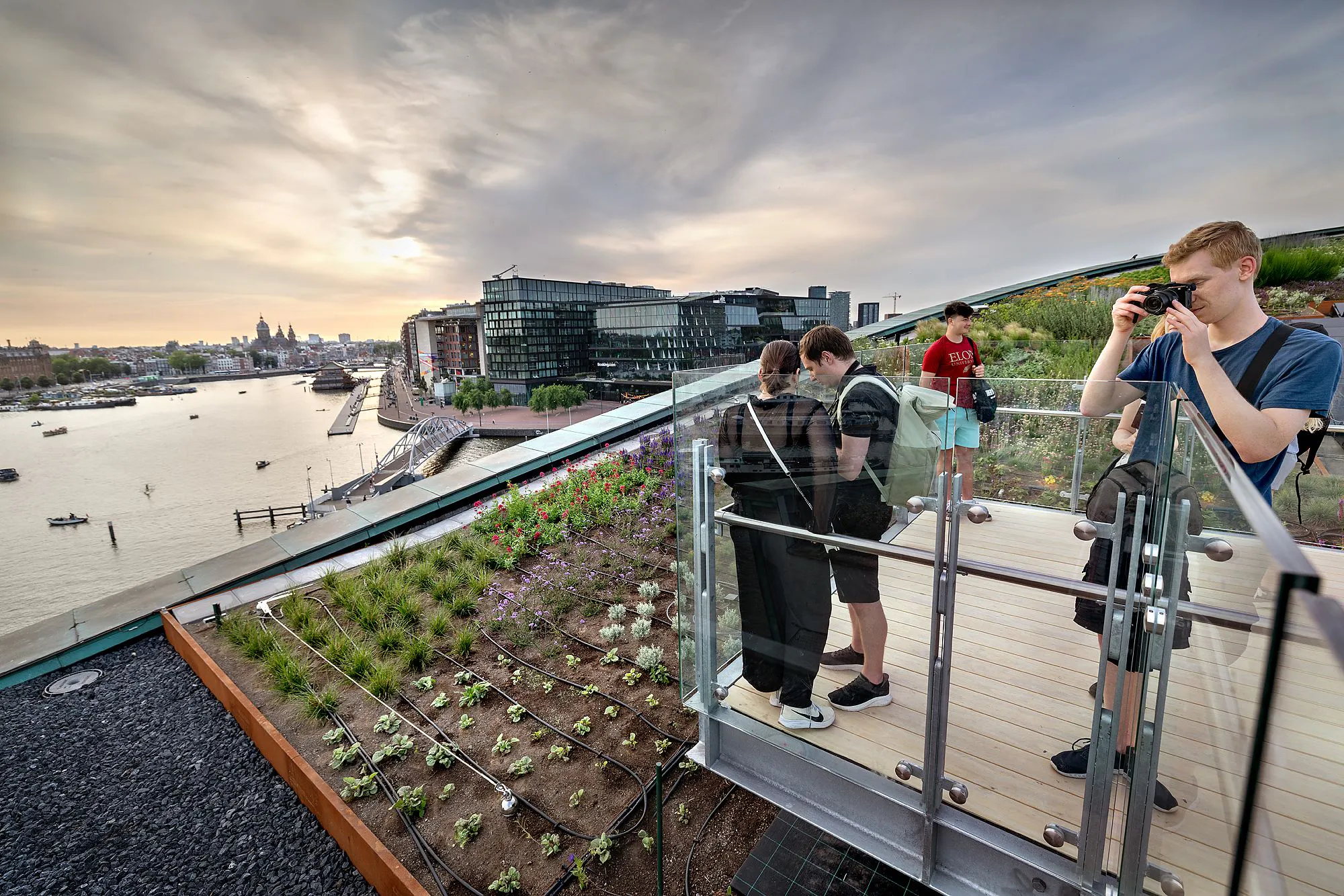 Visitors on the rooftop terrace of NEMO Science Museum, overlooking Amsterdam's cityscape and canal.