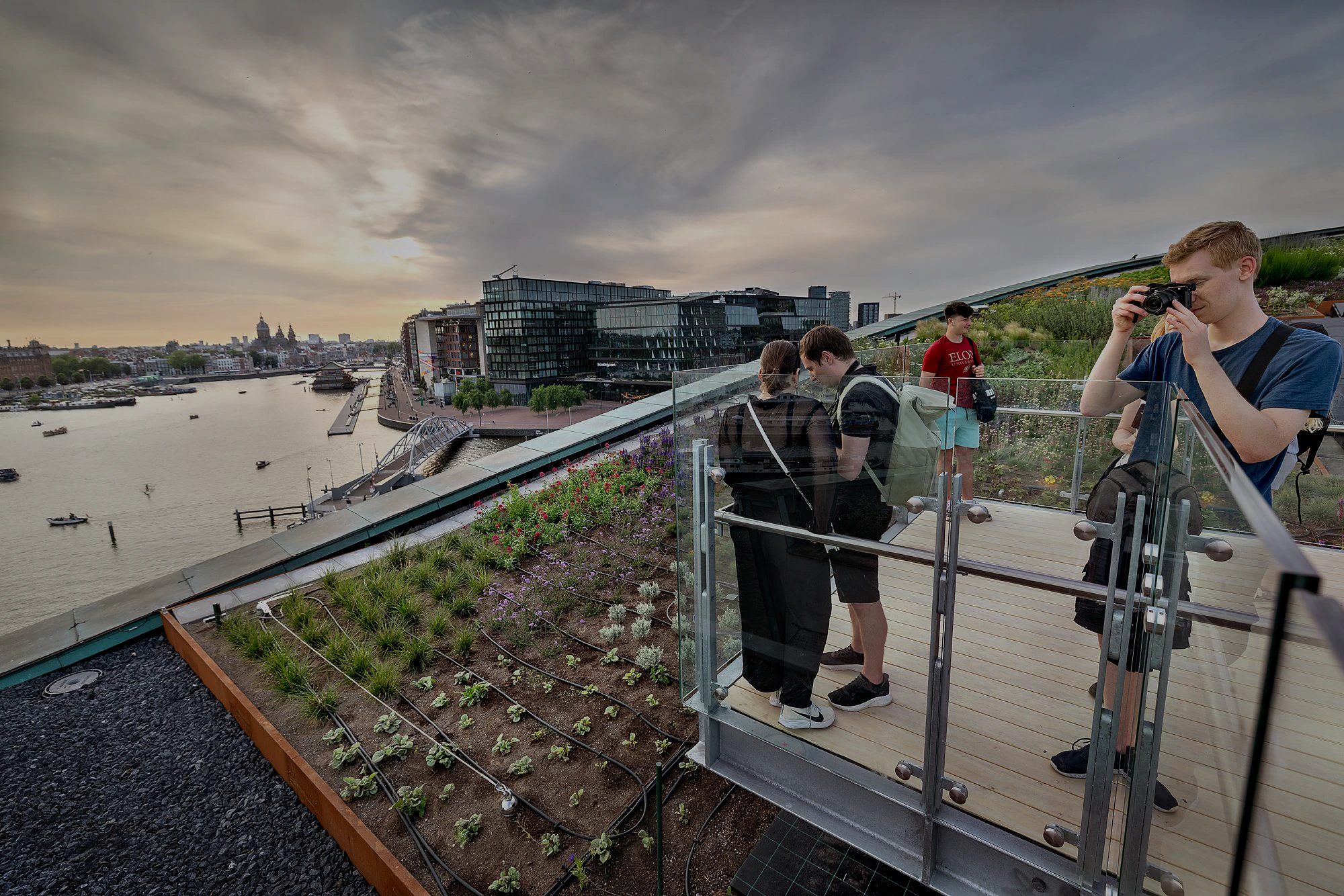 Visitors on the rooftop terrace of NEMO Science Museum, overlooking Amsterdam's cityscape and canal.