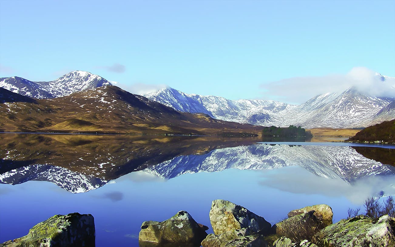 Snow-capped mountains reflecting in Loch Lomond, part of the day tour from Edinburgh.
