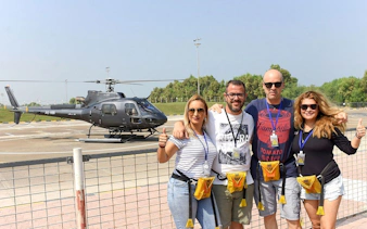 Group of friends posing in front of a helicopter on a sunny day.