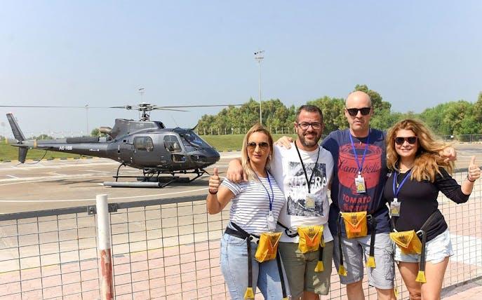 Group of friends posing in front of a helicopter on a sunny day.