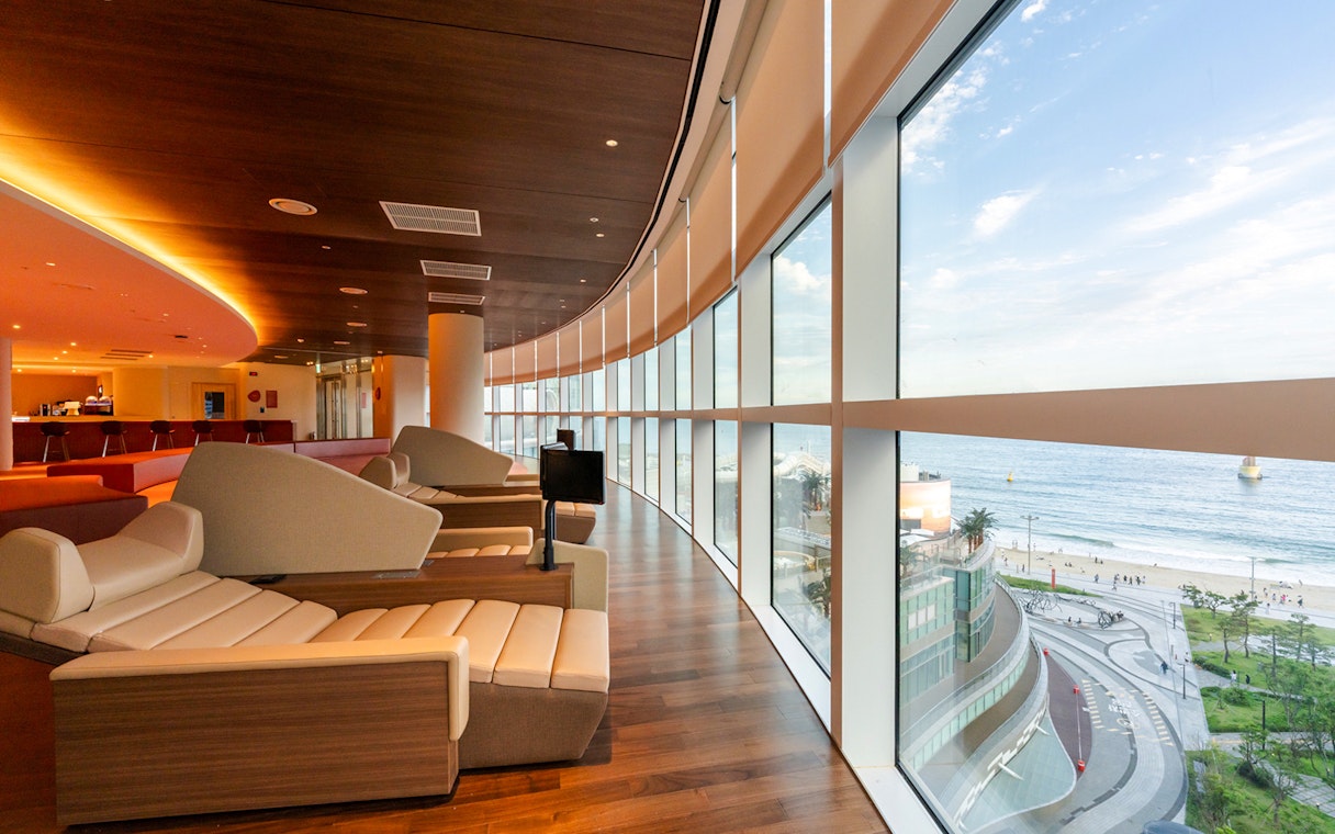Indoor lounge at Club D Oasis with panoramic windows overlooking Haeundae Beach.