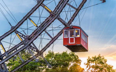 Red cabin on a giant Ferris wheel at sunset, surrounded by trees.