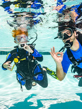 Two scuba divers practicing underwater skills in a swimming pool.