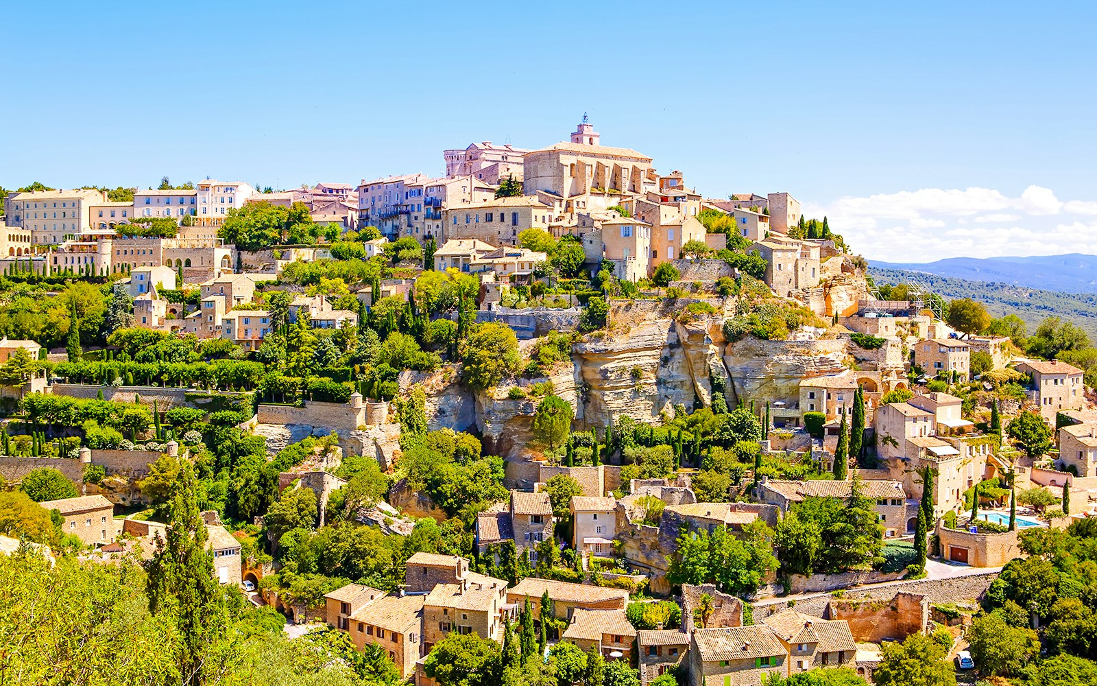 Gordes village view with stone buildings and lush greenery in Provence, France.