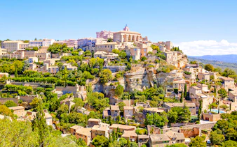 Gordes village view with stone buildings and lush greenery in Provence, France.
