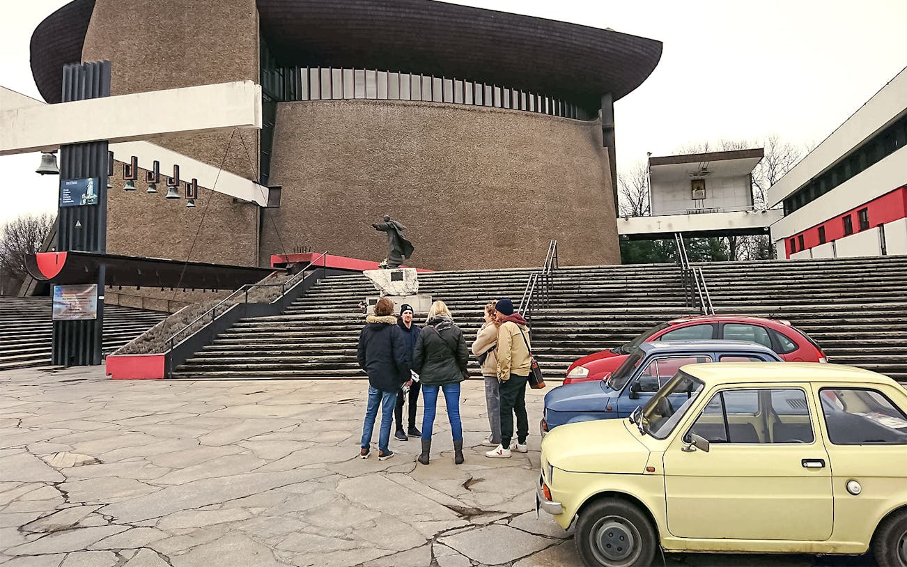 Group touring Nowa Huta in Kraków with retro cars parked nearby.