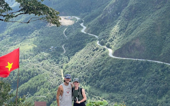 Couple posing with Vietnamese flag overlooking winding mountain road in Sapa on motorbike tour.