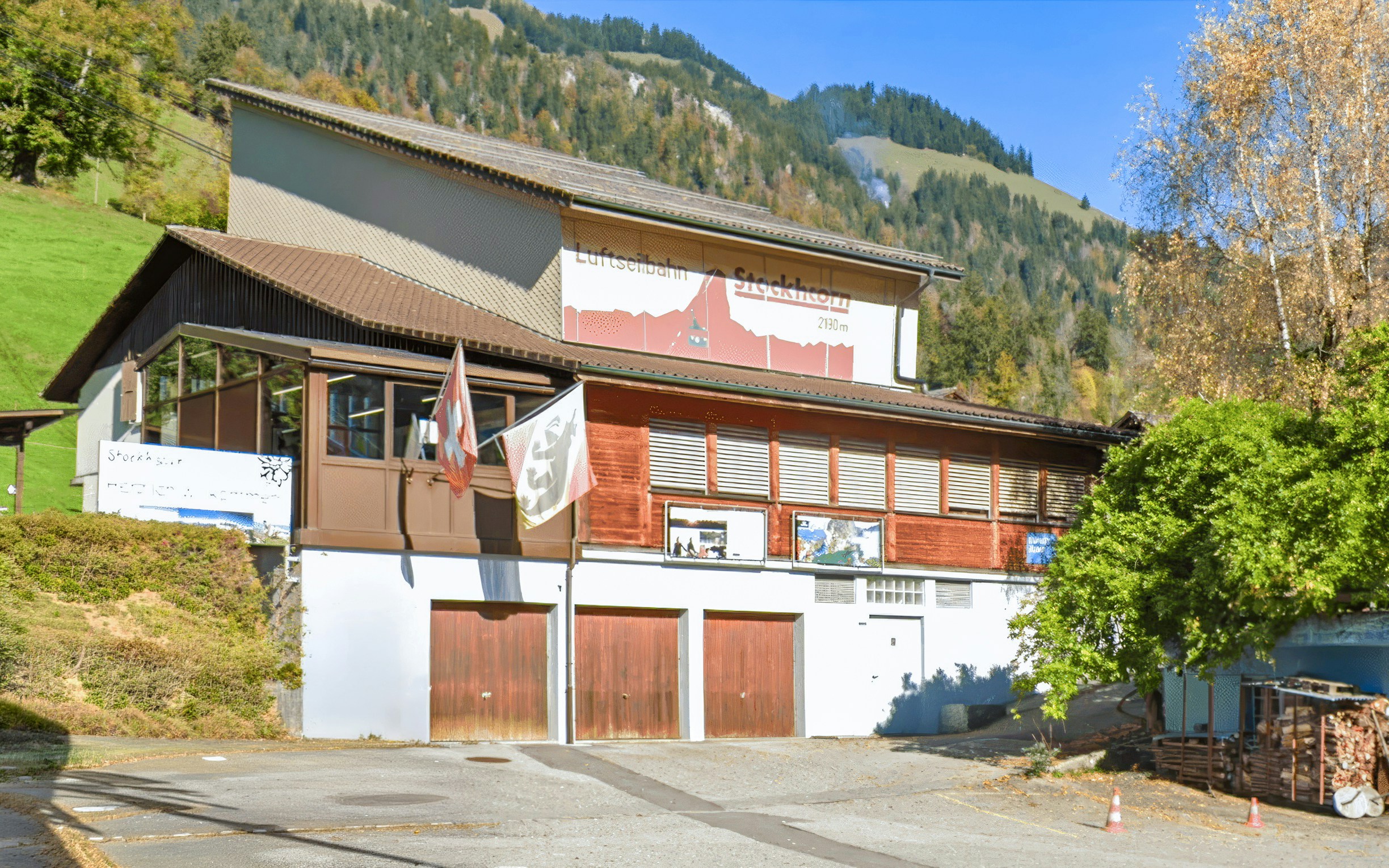 Erlenbach im Simmental valley station building with Swiss flags and mountain backdrop.