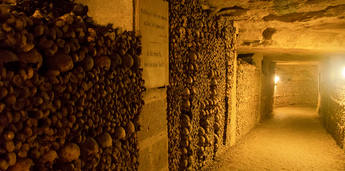Paris Catacombs corridor lined with skulls and bones, dimly lit passageway.